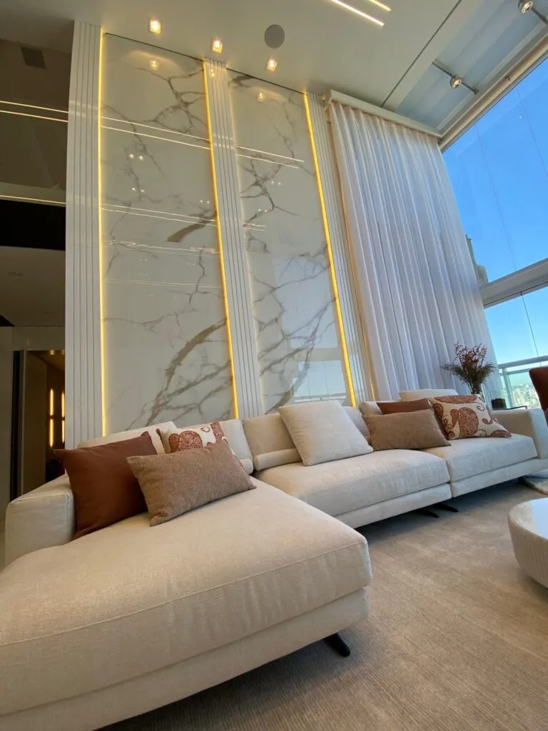 Cortina wave branca em pé-direito duplo com sofá bege e decoração sofisticada, em ambiente de alto padrão.