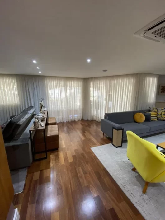 Cortinas wave brancas em living contemporâneo com piso de madeira e sofás modernos, proporcionando leveza e elegância ao ambiente.