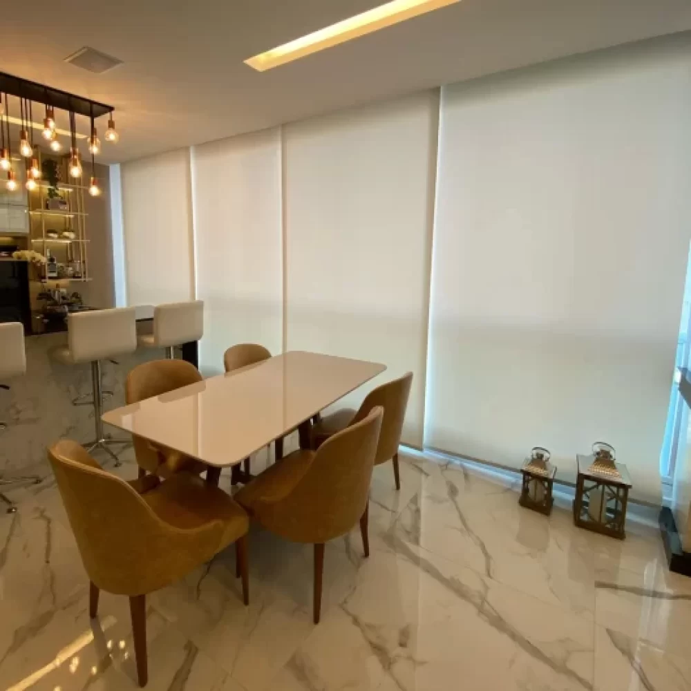Sala de jantar sofisticada com persiana rolô sob medida em tecido branco, projeto da Casa Chic Decor.